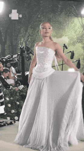 a woman in a white dress stands in front of a camera