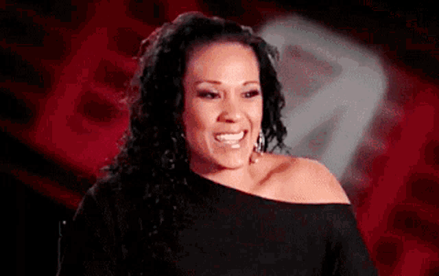 a woman with curly hair is smiling and wearing a black off the shoulder top .