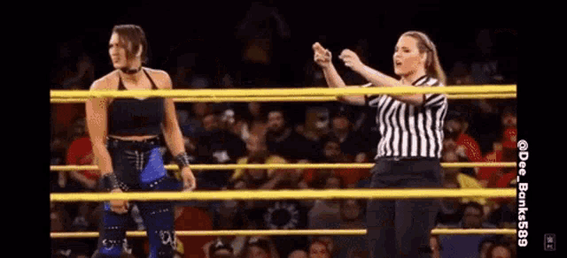 a woman is standing in a wrestling ring with a referee behind her .