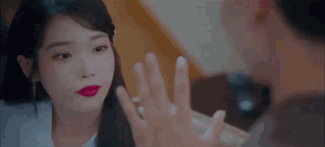 a woman with red lipstick is looking at a man with his hand up .