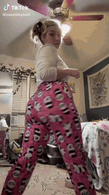 a woman in pink pajamas is standing in a bedroom with a ceiling fan .