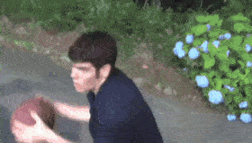 a man in a blue shirt is holding a basketball in front of a bush with blue flowers .