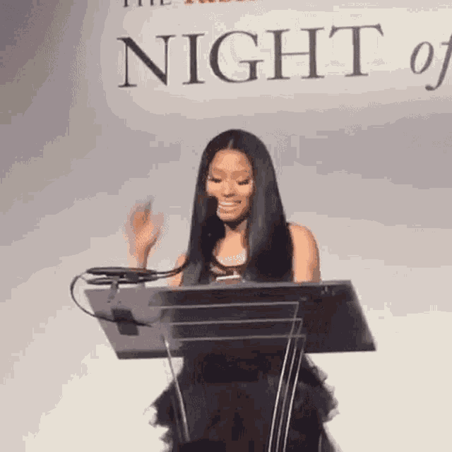 a woman is standing at a podium giving a speech while waving her hand .