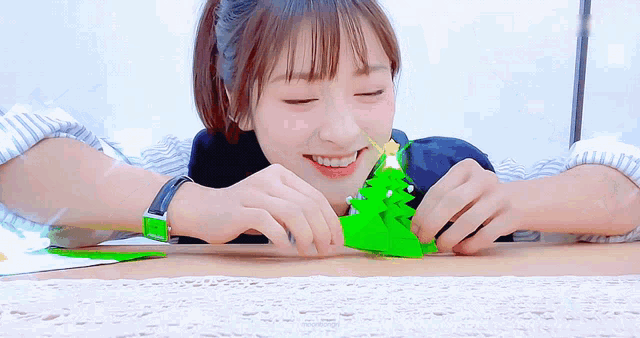 a woman is smiling while holding a green christmas tree in her hands