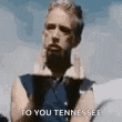 a man with a beard is giving the middle finger while wearing a blue shirt .