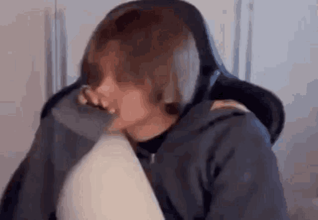 a man in a hoodie is sitting in a chair holding a pillow .