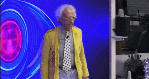 a man wearing a yellow jacket and tie is standing in front of a large eye .