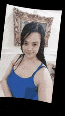 a woman in a blue tank top stands in front of a framed painting
