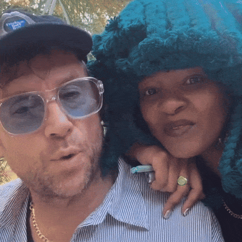 a man and a woman pose for a picture with the man wearing sunglasses and a blue hat that says pepsi