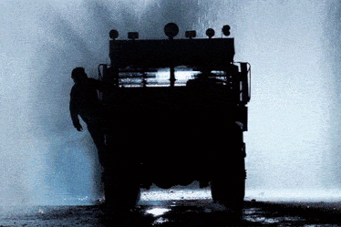 a silhouette of a man standing in front of a military vehicle in the rain