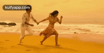 a man and a woman are holding hands and running on the beach .