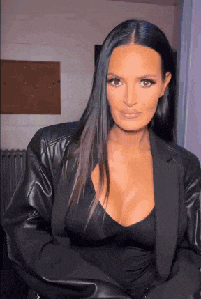 a woman with long black hair and a plunging neckline is wearing a black jacket and a black top .