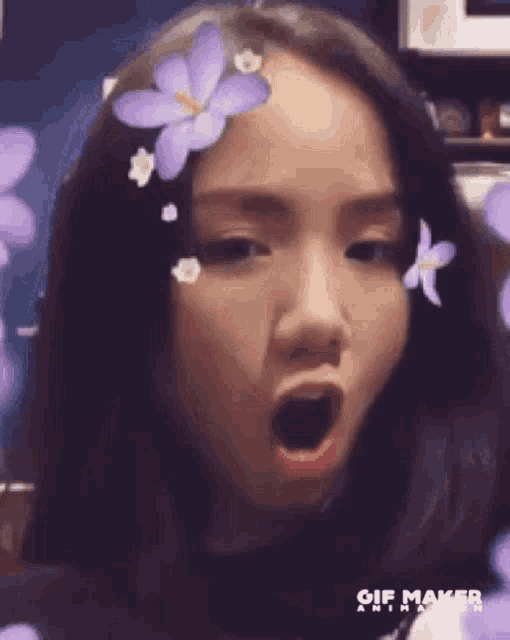 a young woman with purple flowers in her hair is making a funny face .