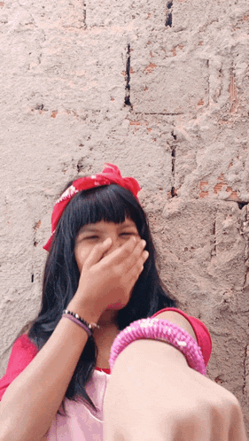 a girl wearing a pink headband and bracelets covering her mouth