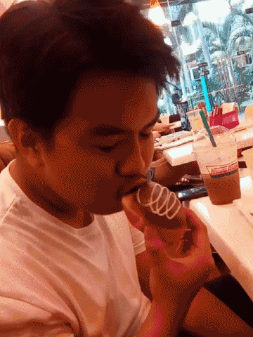 a man in a white shirt is eating a donut and drinking a dunkin donuts cup