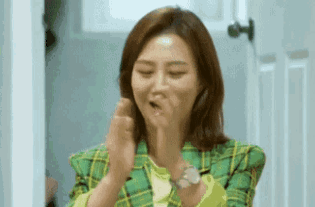 a woman in a green plaid jacket is clapping her hands in front of a door .