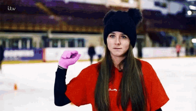 a woman wearing a black hat and pink gloves stands on an ice rink with itv written on the bottom