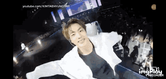 a man in a white jacket is flying through the air on a stage with his arms outstretched .
