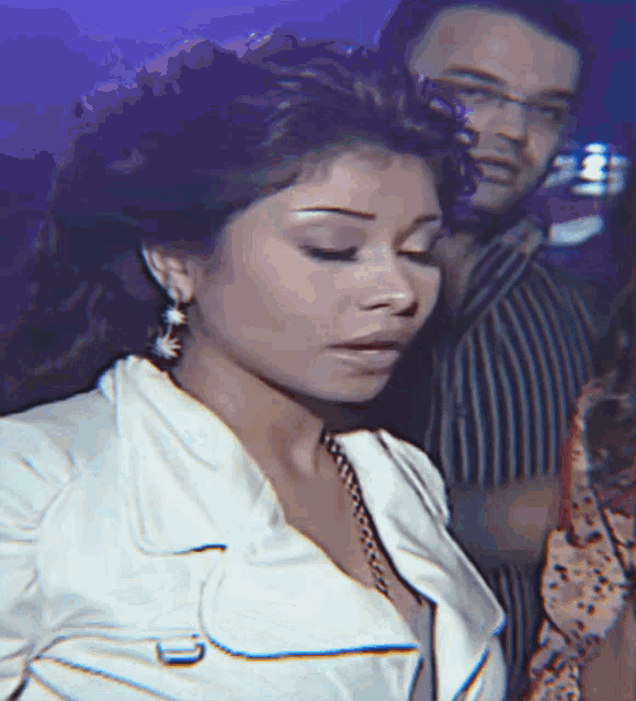 a woman in a white jacket and earrings stands next to a man in a striped shirt