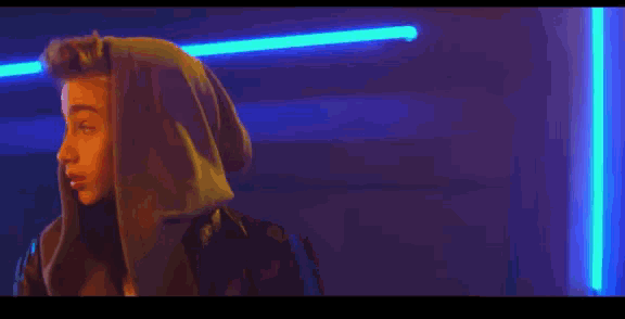 a young man wearing a hooded jacket is standing in a dark room with neon lights .