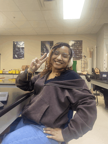 a woman wearing goggles giving a peace sign in a lab