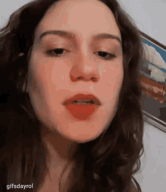 a woman with long hair is making a funny face in front of a picture on a wall .