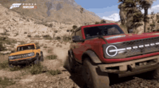 a red ford bronco and a yellow ford bronco are driving down a dirt road