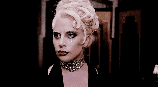 a woman with white hair is wearing a choker and has a tear coming out of her eye .