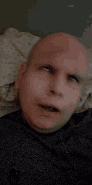 a bald man is laying on a bed with his eyes closed