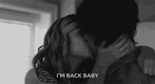 a man and a woman are kissing in a black and white photo with the words `` i 'm back baby '' .