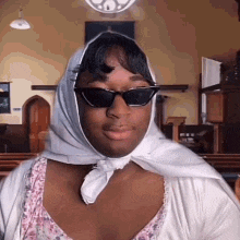 a woman wearing sunglasses and a white scarf around her head is standing in a church .