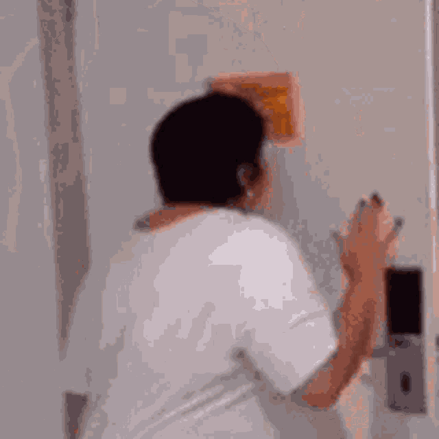 a man in a white shirt is standing in front of a mirror and looking at himself .