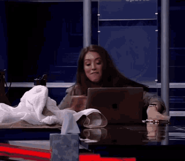 a woman sits at a desk with a laptop and tissues on it
