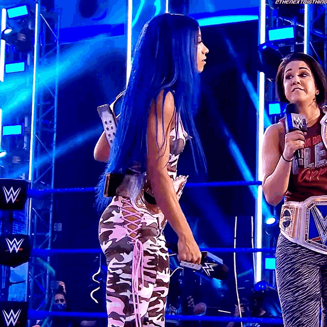 a woman with blue hair is standing in a wrestling ring next to another woman
