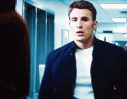 a man in a blue jacket and white shirt is standing in a hallway talking to another man .