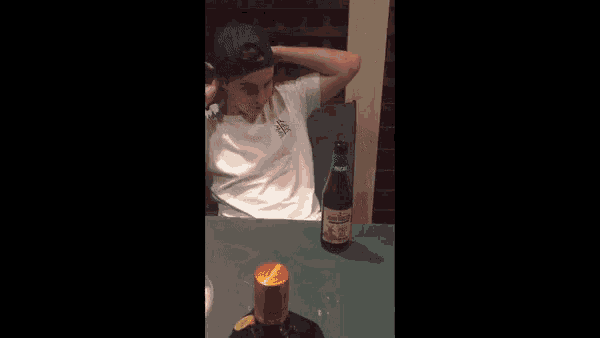 a young man is sitting at a table with a bottle of alcohol and a can of soda .