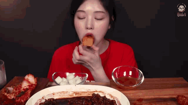 a woman in a red shirt is sitting at a table eating a bowl of food .