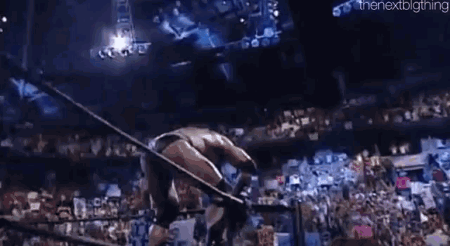 a wrestler is jumping over a rope in a ring in front of a crowd .