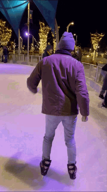 a man in a purple jacket is ice skating on a rink