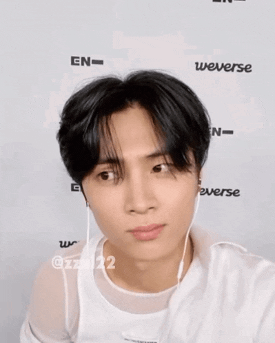 a young man wearing ear buds is standing in front of a wall that says weverse on it