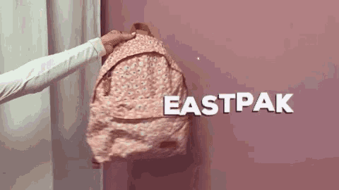 a person is holding a pink eastpak backpack in front of a pink wall