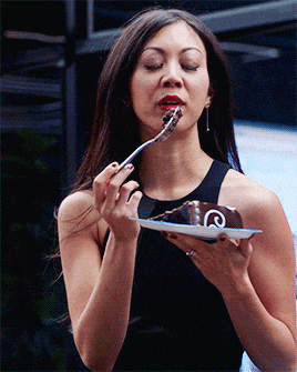 a woman in a black dress is eating a chocolate cake