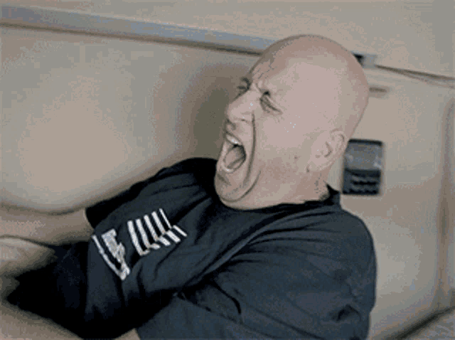 a bald man wearing a black shirt with the word full on it is yawning