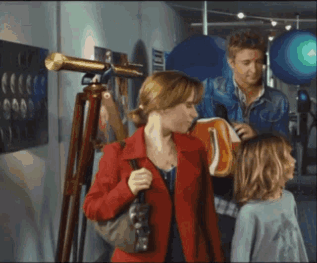 a woman in a red jacket is standing next to a man and a little girl