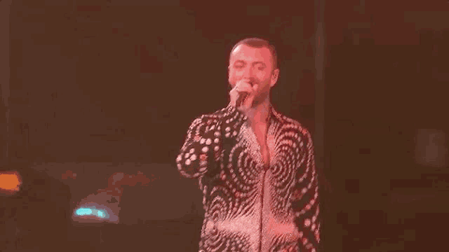 a man in a swirl shirt is singing into a microphone on stage .