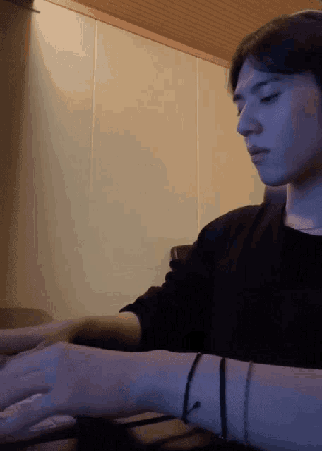 a man in a black shirt is sitting at a table with his hands on a keyboard