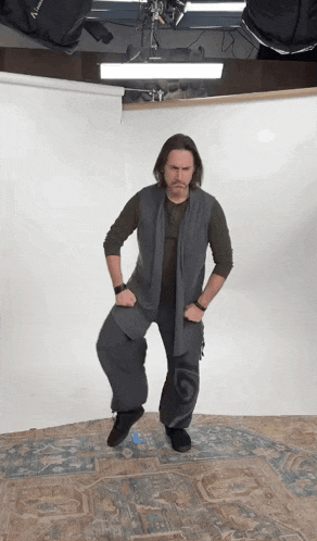 a man in a gray vest and pants is standing with his hands on his hips