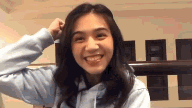 a young woman in a blue hoodie is smiling while holding her hair .