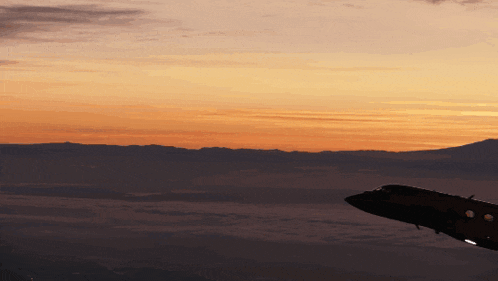 a plane is flying over a cloudy sky at sunset