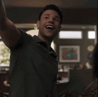 a man in a green shirt is smiling and waving his arm in the air